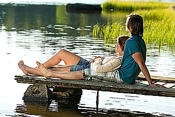 Young Caucasian couple lounging on pier by lake sunset