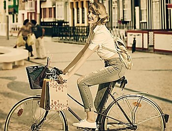 pretty blonde girl with casual dress and backpack going shopping with bicycle. There are some shopping bags in the bike basket