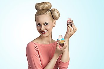 portrait of pretty young girl with funny hair-style and colourful make-up taking two cupcakes in the hands and smiling