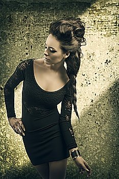 cute brunette girl with cool hair-style and nice make-up wearing dark sexy dress in fashion pose in a grunge old background