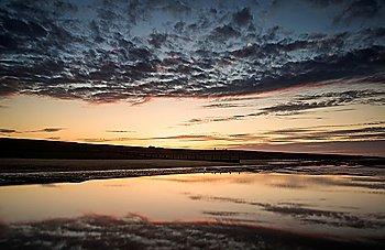 Beautiful sunrise reflected in low tide water pools on beach landscape