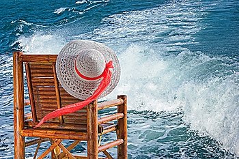 hat hanging on a chair against the sea waves