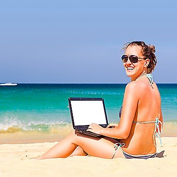working on the beach. Woman is sitting with laptop with blank screen