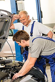 Elderly mechanic supervising young colleague´s work