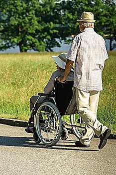 Senior husband pushing wife´s wheelchair in park