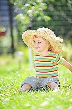 little girl in straw hat sitting on green grass