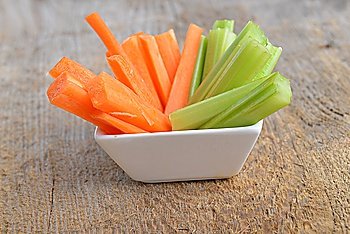 Bowl of carrot and celery sticks on wooden background