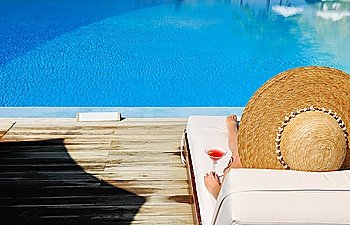 Woman in hat relaxing at the poolside with cosmopolitan cocktail