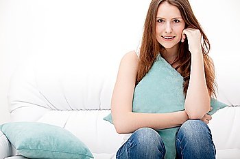 Full-length portrait of a young woman sitting on sofa and hugging her pillow