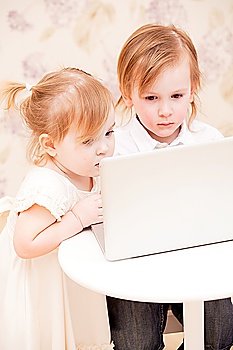Children with laptop indoors. Happy kids playing computer at home.