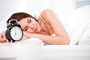 Beautiful sleeping woman resting in bed with alarm clock ready to wake her in the morning