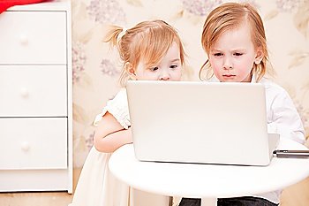 Children with laptop indoors. Happy kids playing computer at home.