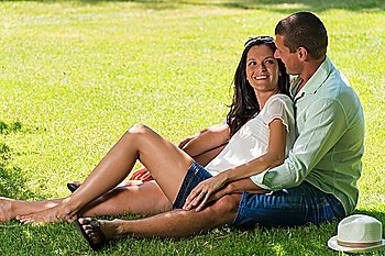 Hugging couple laughing and sitting in grass outdoors