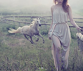 Delicate brunette lady posing with horse in the background