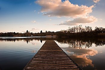 Lovely image of late sunset sky over calm lake landscape with long fishing jetty pier and vibrant colors
