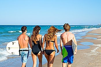 Teen surfers group of boys and girls walking rear view on beach