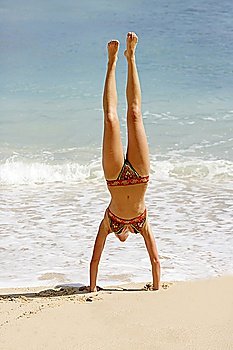 Young woman headstanding on the beach