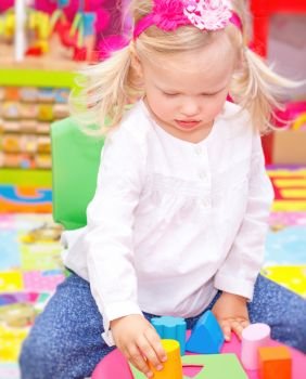 Cute adorable blond baby girl having fun in daycare, playing with colorful toys in playroom, happy healthy childhood