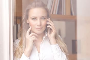 Portrait of a beautiful confident business woman on the phone, standing near windows at the office, young female at work
