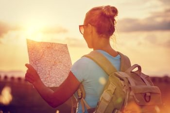 Rear view of a traveler girl with backpack exploring map, enjoying mild sunset light, active people lifestyle, summer fun vacation, traveling around the world 