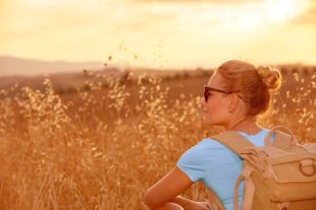 Beautiful traveler girl enjoying golden wheat field in sunset light, beautiful summer nature, farmland in Europe, travel and tourism concept
