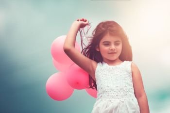 Cute little girl with pink air balloons over blue sky background, enjoying birthday party, happy carefree childhood . Happy girl with air balloons
