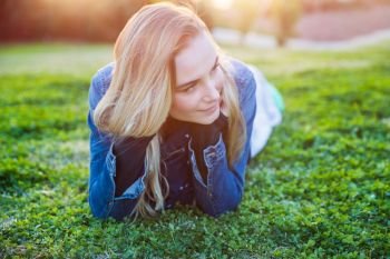 Authentic portrait of a pretty girl lying down on fresh green grass meadow, genuine beauty ofa  young woman, enjoying spring nature and peaceful weekend in countryside 
. Pretty girl lying down on green grass 