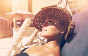 Attractive woman tanning on the beach, lying down on sunbed and taking sun, nice female hides her face from the sun under a straw hat, summer vacation concept                               . Attractive woman tanning on the beach