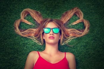 Blond teen girl with hair heart shapes lying down on turf with sunglasses