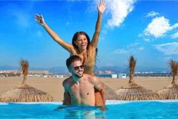Tourist couple piggyback in infinity pool on a beach resort in summer vacation