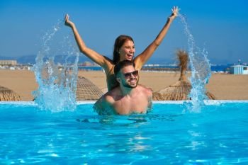 Tourist couple piggyback in infinity pool on a beach resort splashing water