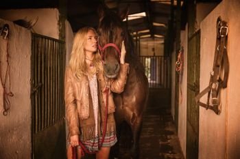 Blond girl holding horse at stable. Blond girl holding horse at stable corridor
