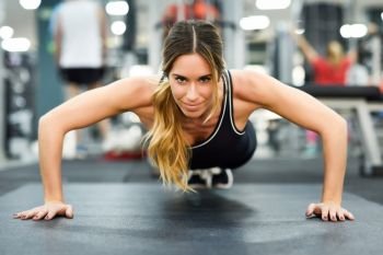 Young beautiful woman doing pushups in the gym. Girl wearing sportwears clothes.