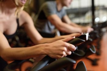 Two people biking in the gym, exercising legs doing cardio workout cycling bikes. Couple in a spinning class wearing sportswear.
