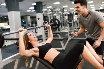 Personal trainer motivating a young woman lift weights while working out in a gym