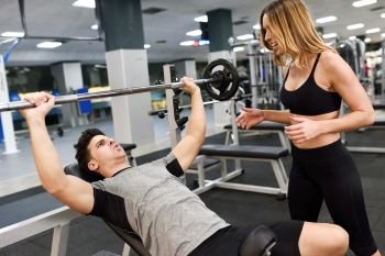 Female personal trainer motivating a young man lift weights while working out in a gym