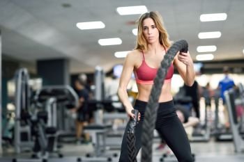 Woman with battle ropes exercise in the fitness gym. Young female wearing sportswear.