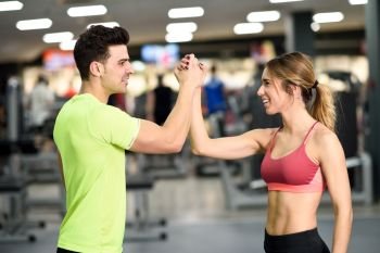 Smiling young man and woman doing high five in gym. Couple wearing sportswear