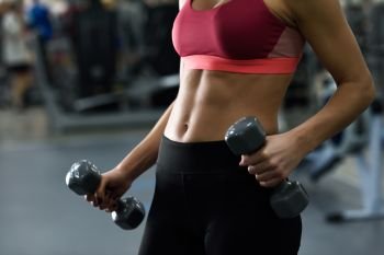 Young woman with beautiful abdomen lifting dumbells at gym. Girl wearing sportswear clothes.