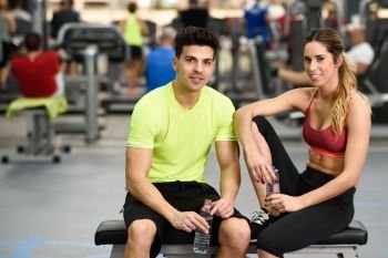 Handsome man and beautiful sporty woman drinking water after workout in the gym
