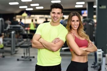 Man and woman personal trainers in the gym. Young girl and guy wearing sportswear with arms crossed.