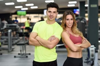 Man and woman personal trainers in the gym. Young girl and guy wearing sportswear with arms crossed.