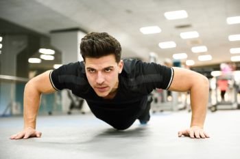 Attractive man doing pushups in the gym. Guy wearing sportwears clothes.