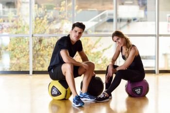 Man and Woman sitting with fitballs in the gym. Young people wearing sportswear clothes.