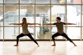 Young woman and man working out indoors. Two people doing exercises. Warrior 2 or Virabhadrasana II pose. 