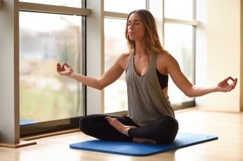 Young beautiful woman meditating in the lotus position in gym. Girl wearing sportswear clothes.