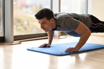 Attractive man doing pushups in the gym on blue mat. Guy wearing sportwears clothes.