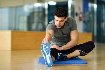 Young man working out indoors. Male stretching their legs on the floor of a gym.