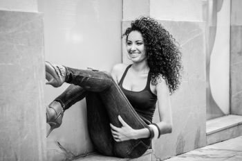 Portrait of a young black woman, afro hairstyle, wearing blue jeans smiling in urban background. Black and white photograph