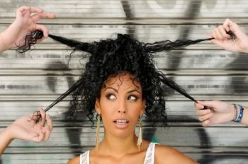 Portrait of a young black woman, afro hairstyle, in urban background with four hands playing with her hair